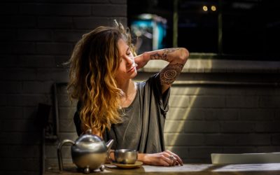 A woman sits in a cosy kitchen drinking a hot drink, she raises her arm as her shoulder range of motion returns.