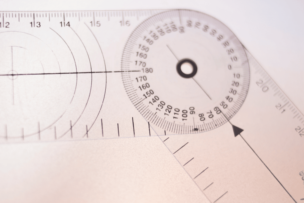 Image shows a goniometer, which is a measurement tool used for measuring shoulder range of motion by physiotherapists. The device looks like two plastic rulers as a sandwich, with a hinge that connects them together. Around the hinge are numbers between 0º and 360º to measure the angle when the two arms of the goniometer are extended to a straight line, doubling its length.